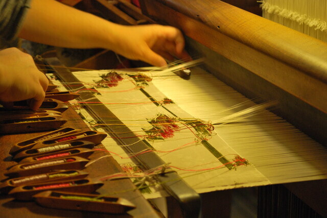 Hands weaving a number of shuttles to make flower-patterned silk