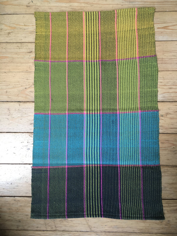 A tea towel with green, lime and pink stripes. The weft has broad stripes of yellow, green, turquoise and navy with pink stripes in between 