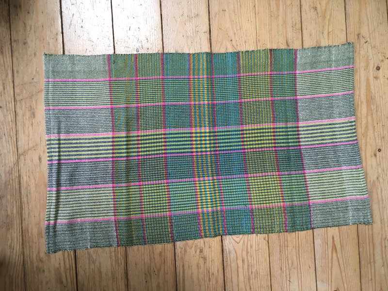 A tea towel with green, lime and pink stripes. Either end is women in white, wit the central section using the same complex pattern of the warp as in the weft.