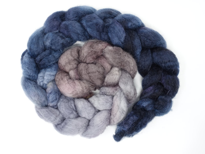 A gradient braid of fibre that transitions from pale brown to grey to blue to french navy.