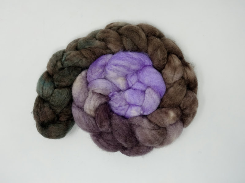A braid of fibre that transitions from pale lavender to brown to dark teal.