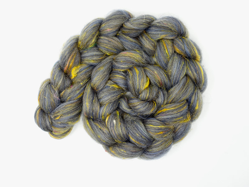 A spiral of combed wool top that's dark blue-grey. There are flecks of golden yellow fibre. 