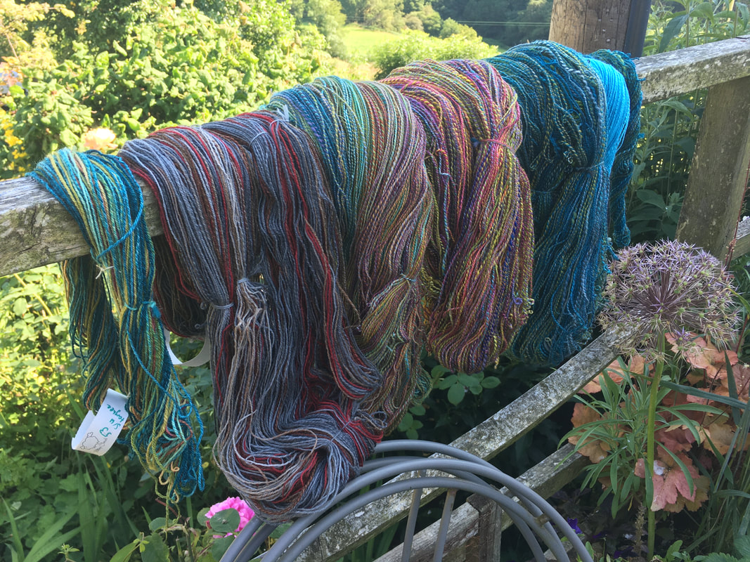 Multicoloured skeins of yarn hang over a wooden railing. 