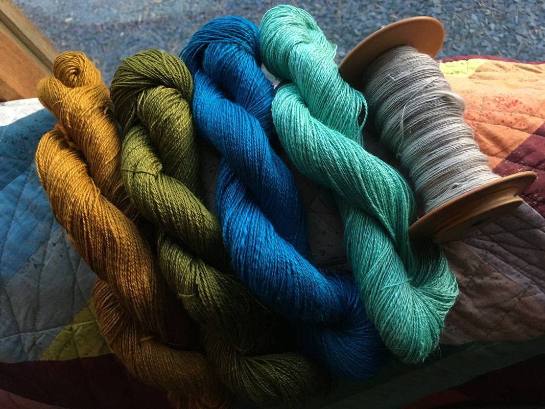 4 skeins of handspun ramie, in a light fingering weight. One is golden yellow, the next is olive green, then turquoise and mint green. There's also a bobbin of cotton singles in pale grey. 