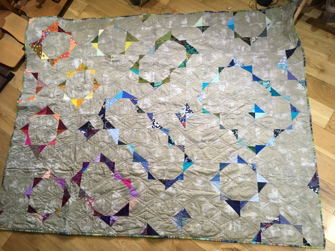A beige quilt with linear rectangles of different colours made by cutting the corners off squares and then arranging them to make continual lines