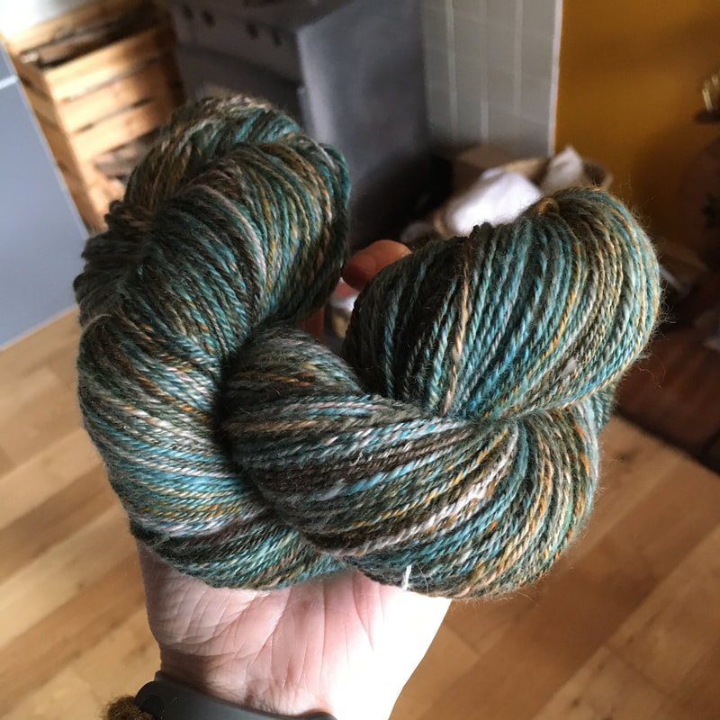 A skien of 3-ply cashmere yarn in a hand. The yarn is turquoise, ochre and brown. 